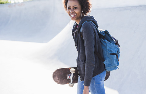 Glückliche junge Frau mit Skateboard, die Musik hört, lizenzfreies Stockfoto