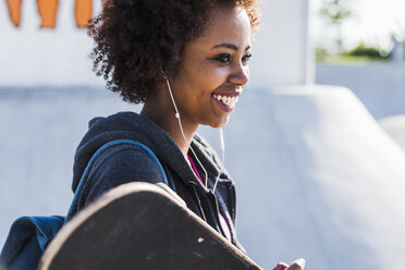 Lächelnde junge Frau mit Skateboard, die Musik hört - UUF007260