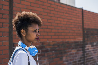 Young woman wearing headphones in front of brick wall - UUF007305