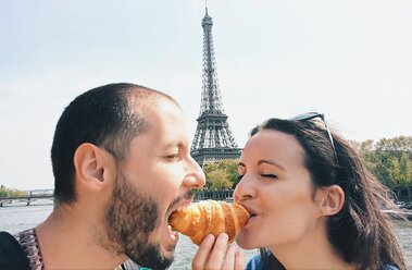 Paris, Frankreich, Verliebte essen ein Croissant in der Nähe des Eiffelturms - GEMF000907