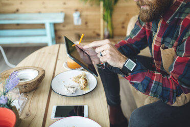 Mann sitzt in einem Café und benutzt ein digitales Tablet - DAPF000101