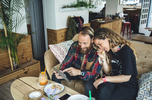 Ehepaar frühstückt in einem Café und schaut auf einen Tablet-PC - DAPF000103