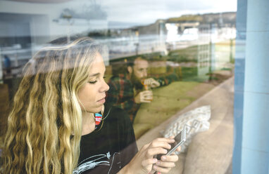 Porträt einer blonden Frau mit Blick auf ihr Smartphone in einem Café - DAPF000105