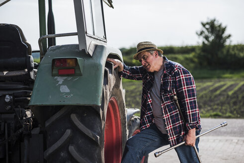 Landwirt hält Werkzeug und untersucht einen Traktorreifen - UUF007333