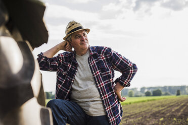 Landwirt lehnt sich auf einem Feld an einen Traktor - UUF007349