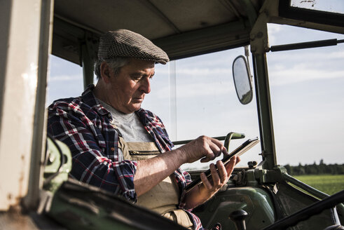 Landwirt sitzt im Traktor und benutzt ein digitales Tablet - UUF007361