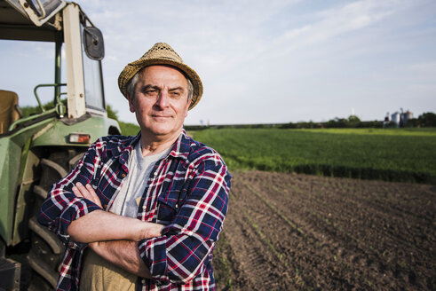 Landwirt steht neben einem Traktor auf einem Feld - UUF007366