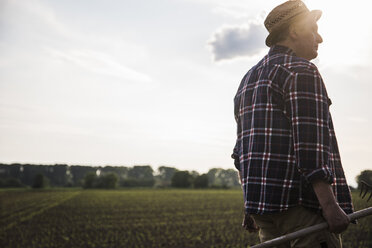 Landwirt hält Rechen neben einem Feld - UUF007367