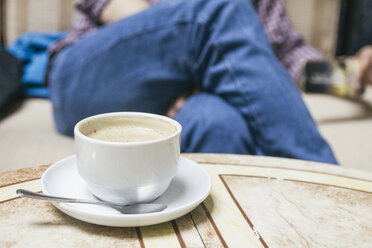 Cup of coffee on a table with man sitting in the background - ABZF000527