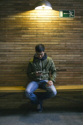 Mann sitzt auf einer Bank und schaut auf sein Smartphone - ABZF000531