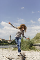 Italien, Verona, Frau balanciert auf Totholz am Flussufer - GIOF001035