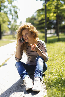 Porträt einer glücklichen Frau, die mit ihrem Smartphone in einem Park telefoniert - GIOF001048