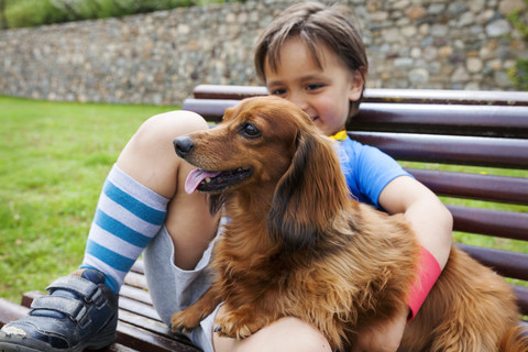 Kleiner Junge mit Hund auf einer Bank sitzend, lizenzfreies Stockfoto