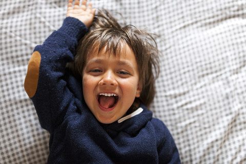 Glücklicher kleiner Junge auf dem Bett liegend, lizenzfreies Stockfoto