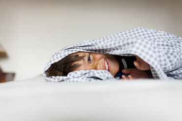 Lächelnder kleiner Junge, der unter der Decke in seinem Bett liegt - VABF000509