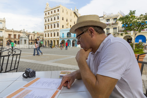 Kuba, Havanna, Tourist sitzt im Straßencafé und schaut auf die Menükarte, lizenzfreies Stockfoto