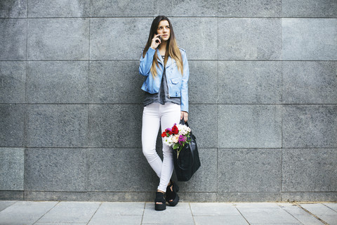 Junge Frau am Handy mit Blumenstrauß in ihrer Tasche, lizenzfreies Stockfoto