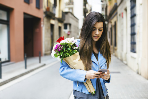 Junge Frau mit Mobiltelefon und Blumenstrauß in der Stadt, lizenzfreies Stockfoto