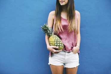 Junge Frau steht mit Ananas an blauer Wand - EBSF001376