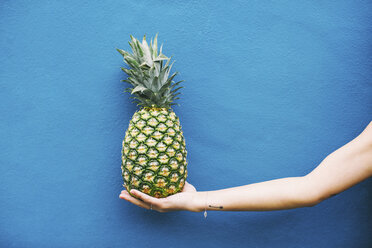 Woman holding pineapple at blue wall - EBSF001379