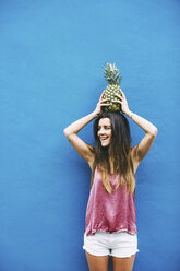 Lächelnde junge Frau hält Ananas an blauer Wand - EBSF001380