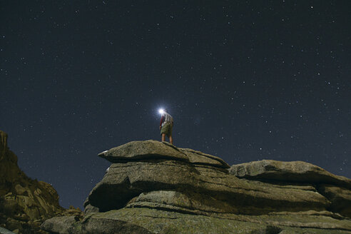 Spanien, Mann mit Stirnlampe unter einem Sternenhimmel auf einem Felsen in La Pedriza - ABZF000532