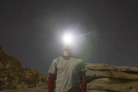 Mann mit Stirnlampe unter einem Sternenhimmel, lizenzfreies Stockfoto