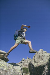 Spanien, Wanderer mit Rucksack springt auf die Felsen in La Pedriza - ABZF000538