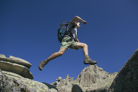 Spanien, Wanderer mit Rucksack springt auf die Felsen in La Pedriza, lizenzfreies Stockfoto