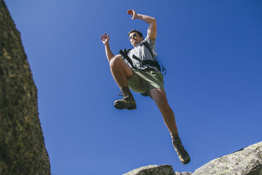 Spanien, Wanderer mit Rucksack springt auf die Felsen in La Pedriza - ABZF000542