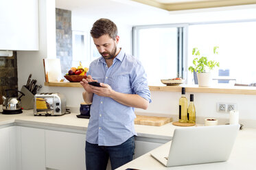 Mann arbeitet in der Küche und benutzt ein Smartphone - HAPF000381