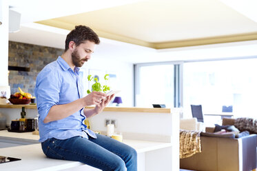 Man sitting in kitchen using smart phone - HAPF000386