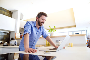 Man working in kitchen using laptop - HAPF000394