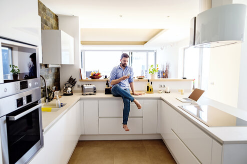 Man sitting in kitchen using smart phone - HAPF000398