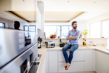 Man sitting in kitchen with arms crossed - HAPF000399