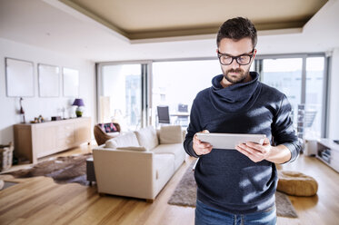 Man standing in living room, using digital tablet - HAPF000415