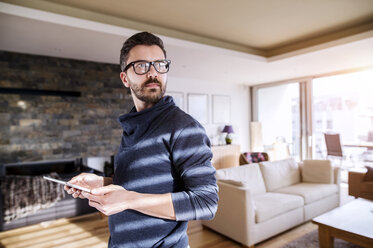 Man standing in living room, using digital tablet - HAPF000418