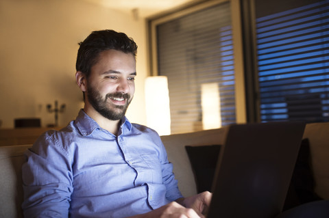 Mann sitzt auf dem Sofa und benutzt einen Laptop, lizenzfreies Stockfoto