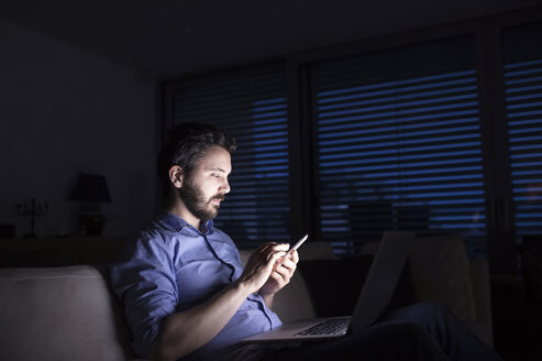 Man working at night using smart phone and laptop - HAPF000426