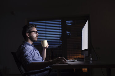 Mann arbeitet am Computer und trinkt nachts Kaffee - HAPF000430