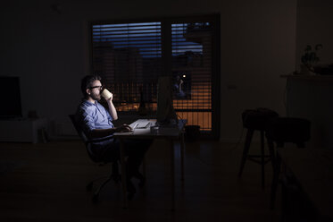 Man working at computer and drinking coffee at night - HAPF000431