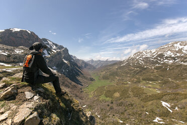 Spanien, Asturien, Somiedo, Mann betrachtet die Landschaft auf einem Berggipfel sitzend - MGOF001852
