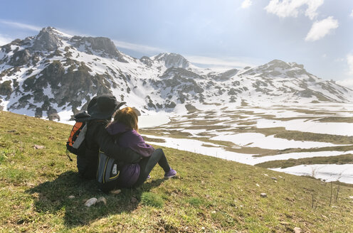 Spanien, Asturien, Somiedo, Paar, das auf einer Wiese sitzend die Landschaft betrachtet - MGOF001864