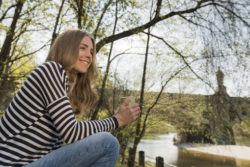 Lächelnde junge Frau im Freien mit einer Tasse Kaffee - KAF000142
