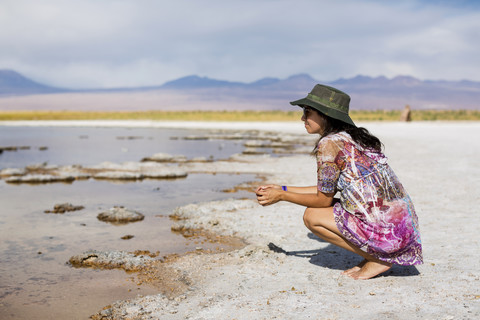 Chile, San Pedro de Atacama, Frau hockt in der Wüste am Seeufer, lizenzfreies Stockfoto