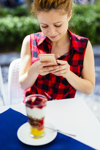 Frau in einem Straßencafé schaut auf ihr Handy, lizenzfreies Stockfoto