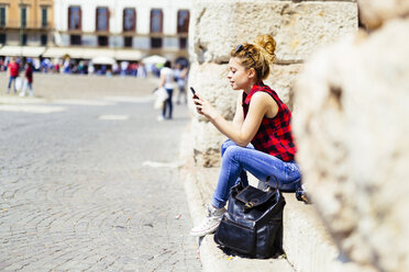 Italy, Verona, woman sitting on stairs looking at cell phone - GIOF001059