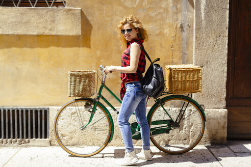 Lächelnde Frau mit Fahrrad in einer Gasse - GIOF001079