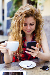 Frau in einem Straßencafé schaut auf ihr Handy - GIOF001081