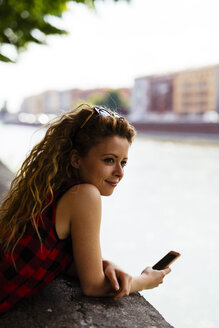 Italien, Verona, Frau am Flussufer mit Mobiltelefon - GIOF001087